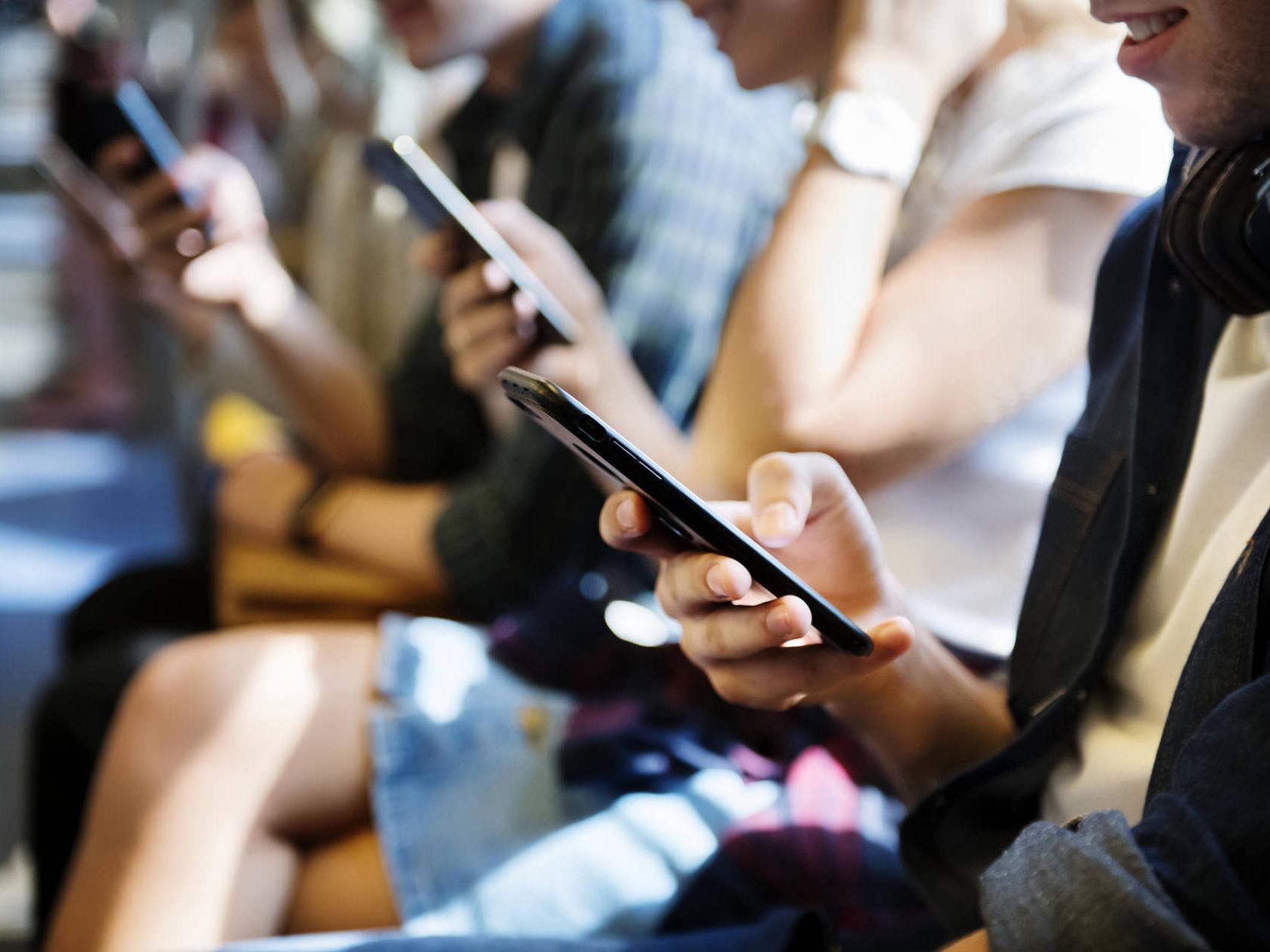 Smartphones emit high levels of blue light. Pictured are multiple people looking at smartphones. 