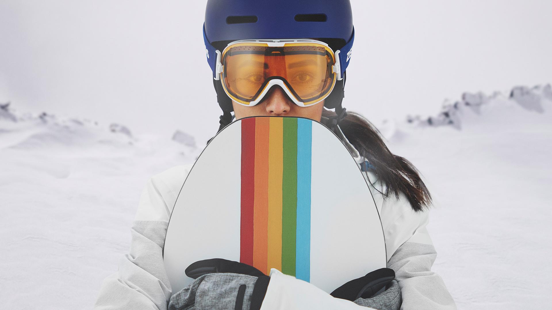 A young women wearing snow goggles with ZEISS Interchangeable technology and hold a snowboard.