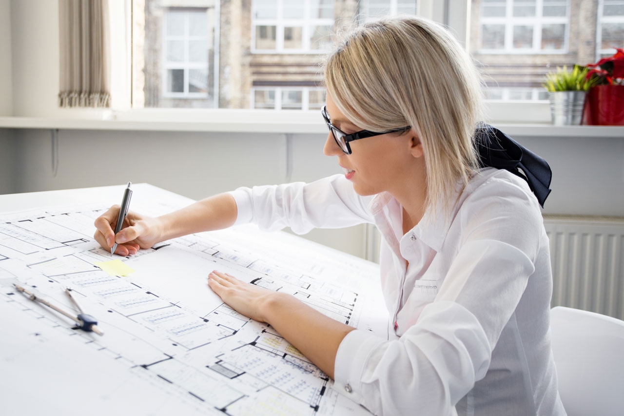 Young female architect with glasses working on blueprint