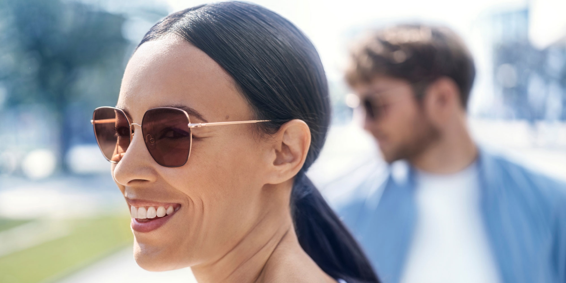 Front: smiling woman with sunglasses, background: a man with glasses